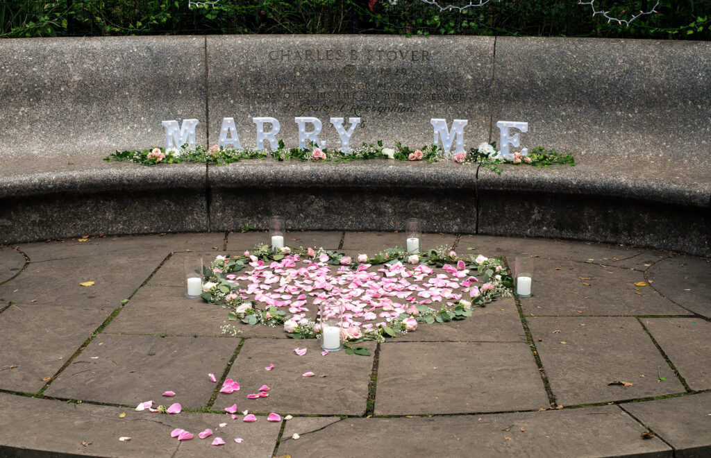 Marry Me sign with pink rose petals in a tucked-away rotunda within Shakespeare Garden in Central Park.