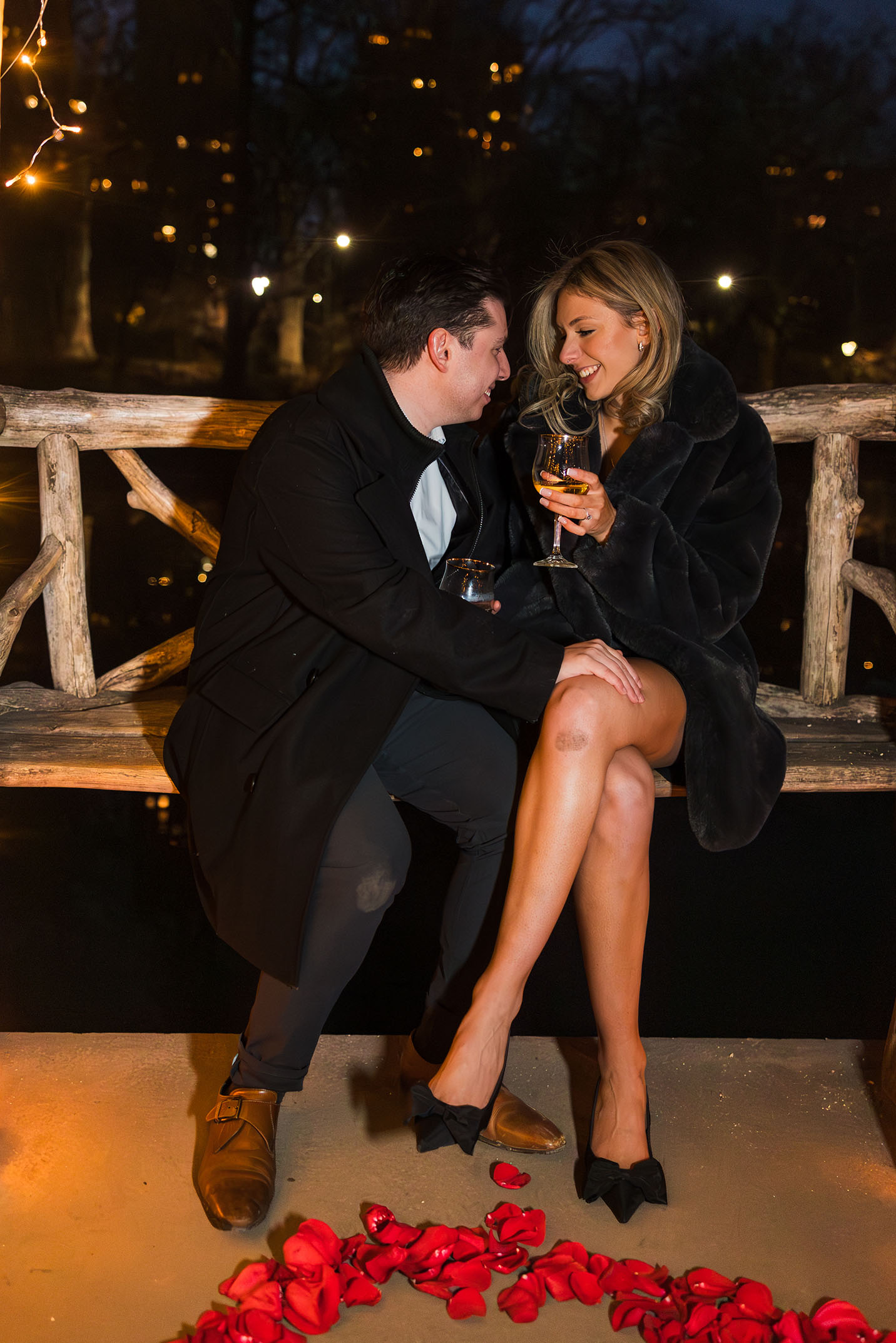 A newly engaged couple celebrating with wine by the water at Wagner's Cove in Central Park.