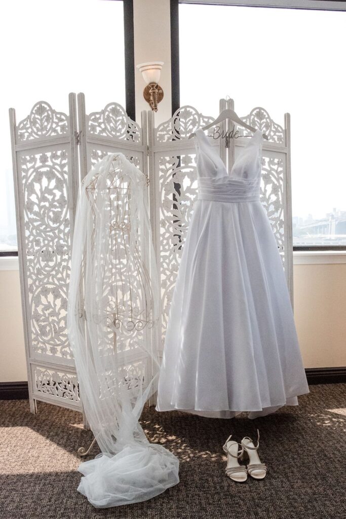 Wedding dress hanging on carved white folding screen with veil and shoes styled nearby.
