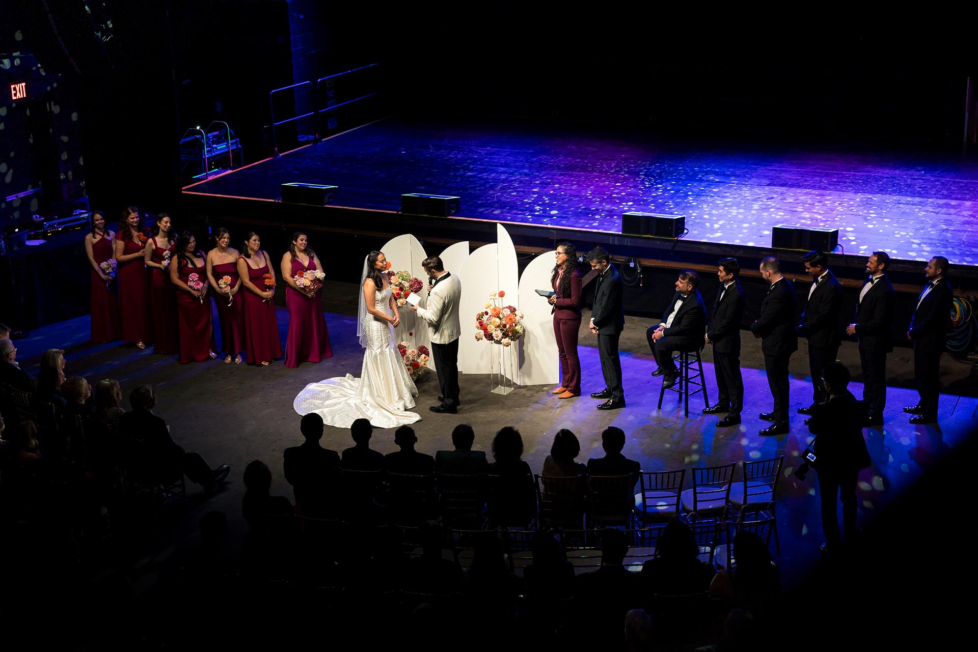 Wedding ceremony at Brooklyn Steel in NYC, with bride, groom, bridal party, officiant, bridal party and their ceremony floral pillars.