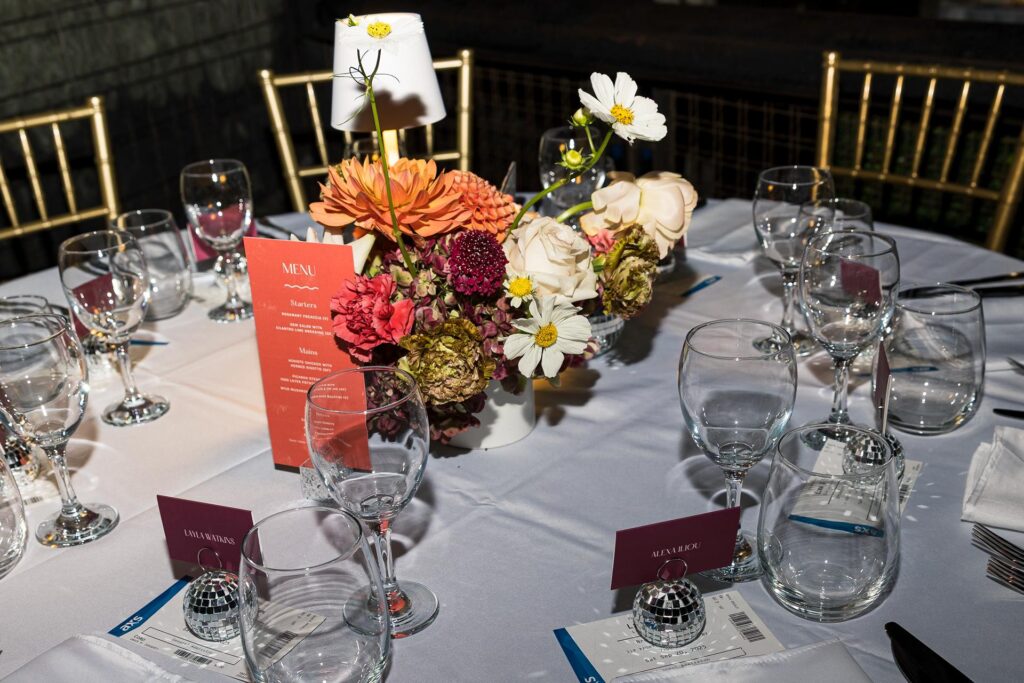 Reception tablescape with disco themed flowers, lamps, menu and talbe names held by disco balls,photographed with flash.