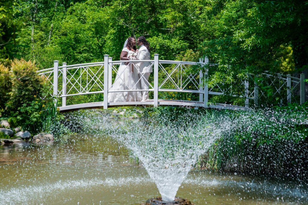 Couple on a suspension bridge with fountain, trees and greenery in New Jersey, photographed during their wedding
